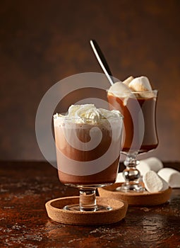 Hot chocolate with whipped cream in a glass mug on a old brown table