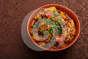 hot cholent sprinkled with green onions in a clay plate on the table