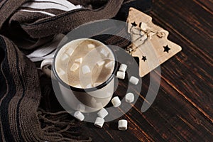 Hot Christmas drink with marshmallows in an iron mug, on a wooden table and a scarf. New Year, holiday background, greeting card