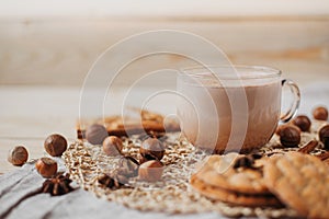 Hot cocoa with cookies, cinnamon sticks, anise, nuts on wooden background