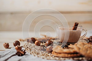 Hot cocoa with cookies, cinnamon sticks, anise, nuts on wooden background