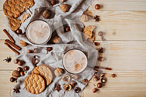 Hot cocoa with cookies, cinnamon sticks, anise, nuts on wooden background