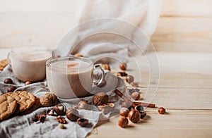 Hot cocoa with cookies, cinnamon sticks, anise, nuts on wooden background