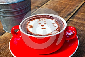 Hot cocoa and face cat milk foam in the red cup on wood background