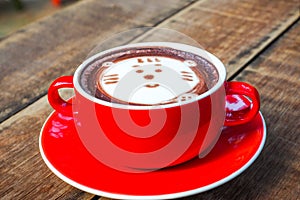 Hot cocoa and face cat milk foam in the red cup on wood background