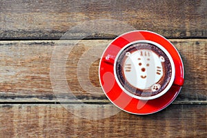 Hot cocoa and face cat milk foam in the red cup on wood background