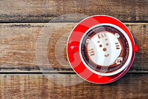 Hot cocoa and face cat milk foam in the red cup on wood background