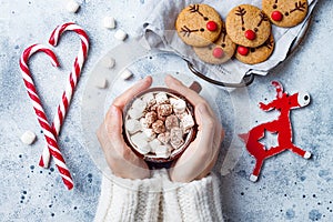 Hot cocoa with marshmallow in in woman hand. Christmas gingerbread, decorated red nosed reindeer cookies. photo