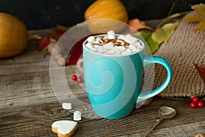 Hot cocoa with marshmallows in a blue ceramic mug with autumn leaves and pumpkins on a wooden table. The concept of hygge, cozy