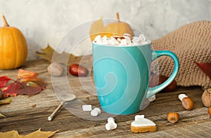 Hot cocoa with marshmallows in a blue ceramic mug with autumn leaves and pumpkins on a wooden table. The concept of hygge, cozy