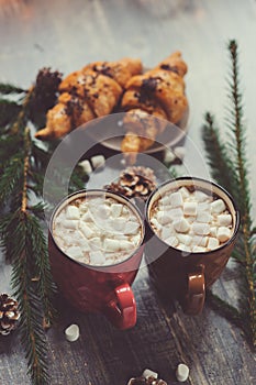 Hot cocoa with marshmallows and croissant on rustic wooden table with christmas lights