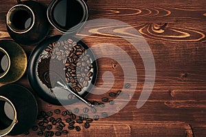 Hot coffee in black cup and turkish pots cezve with beans, saucer with copy space on brown old wooden board background, top view.