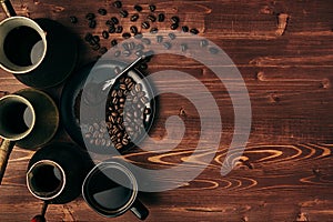 Hot coffee in black cup and turkish pots cezve with beans, saucer with copy space on brown old wooden board background, top view.