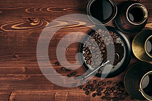 Hot coffee in black cup and turkish pots cezve with beans, saucer with copy space on brown old wooden board background, top view.