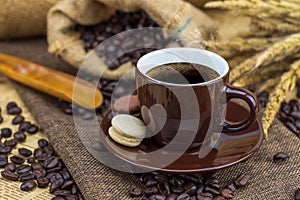 Hot coffee in brown cup with beans, saucer and macarons