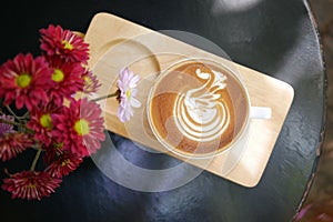 Hot coffee cappuccino latte art swan bird foam on wooden plate with flowers top view background.