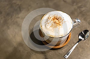 Hot coffee cappuccino with milk foam froth cover on top,sprinkled with chocolate powder or cinnamon,on cement background at coffee