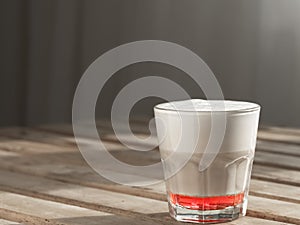 Hot coffee cappuccino with raspberry syrup in glass with milk foam on wooden table. Shallow depth of field, focus on the cup.