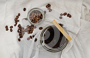 Hot coffee in clear glass serve with thai dessert crispy stick sweet with roasted coffee beans nearby on white background