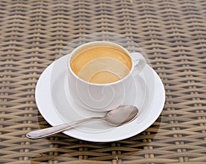 Hot Coffee cream in white cup with tea spoon on wooden table.