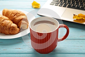 Hot coffee with croissant and autumn leaves on blue - seasonal relax concept