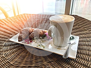 Hot coffee with croissants decorate with flower on rattan table