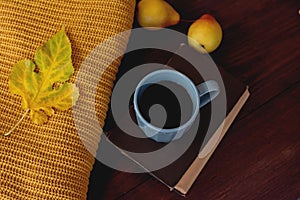 Hot coffee cup, book, fall light brown leaves, knitted sweaters on a table. Aesthetic autumn still life