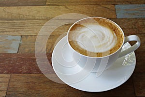 Hot coffee cup cappuccino or latte with stirred spiral milk foam on multicolor plank wood table background in the morning