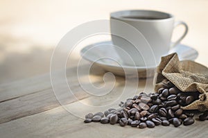 Hot coffee cup and coffee beans roasting on the wooden table in the morning