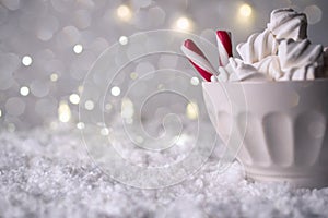 Hot Coffee cup with marshmallows and red candy cane on a frosty winter background. Christmas holidays background.