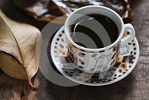 Hot coffee in the cup on old wood table with leaf