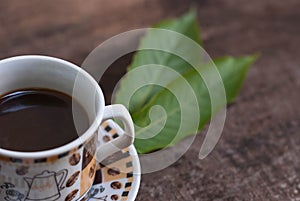 Hot coffee in the cup on old wood table with leaf