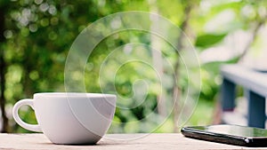 Hot coffee cup steaming on wooden table and green garden background