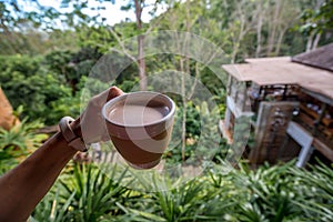 Hot Coffee in a Cup was holding by left hand in front of landscape mountain view