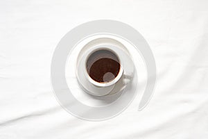 Hot coffee cup in white ceramic mug placed on white tablecloths., top view.