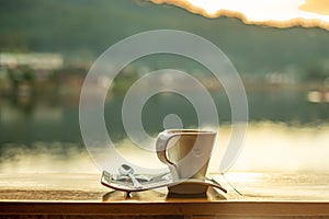 Hot coffee cup on wood table against lake view background at coffee shop in the morning sunrise, Ban Rak Thai village, Mae Hong