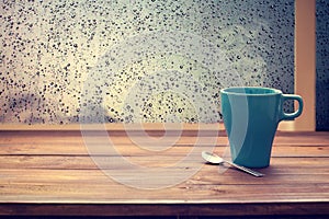 Hot coffee cup on wood table with raindrop window,