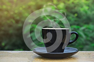 Hot coffee, heart shape smoke in black ceramic cup on wooden table in coffee shop and cafe with green background and flare light,