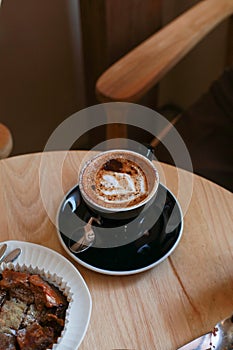 Hot coffee with latte art in black ceramic cup on wooden table. Cappuccino or latte with frothy foam milk.