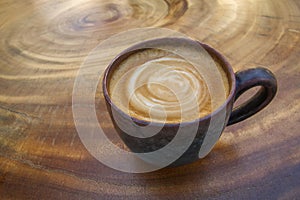 Hot coffee latte cappuccino with spiral milk foam in vintage ceramic cup on wood texture background.