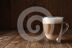 Hot coffee with milk in glass cup on wooden table. Space for text