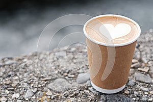 Hot coffee paper cup against river background, heart shape latte coffee art. Love, holiday, Valentine day and free plastic