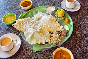 Hot coffee and plate with South Indian food thali with rice and spicy vegetables, on palm leaf in indian cafe.