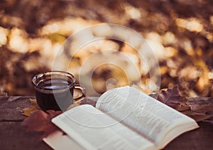 Hot coffee and red book with autumn leaves on wood background - seasonal relax concept