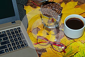 Hot coffee in red cup with steam and eyeglasses on stacked books with laptop on wooden background, coffee break concept