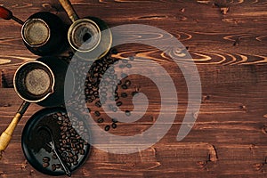 Hot coffee in shabby turkish pots cezve with beans, saucer with copy space on brown old wooden board background, top view.