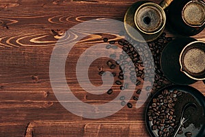 Hot coffee in shabby turkish pots cezve with beans, saucer with copy space on brown old wooden board background, top view.