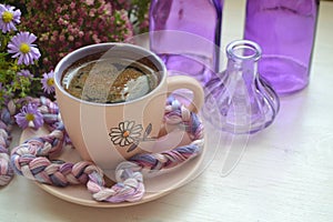 Hot coffee in a vintage cup and on an old white wooden background with violet flowers and purple bottles