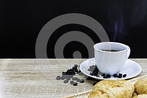 Hot coffee in white cup with coffee bean and croissants on wooden table