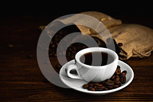 Hot coffee in a white coffee cup and many coffee beans placed around on a wooden table in a warm, light atmosphere, on dark